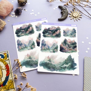 May include: Two sheets of stickers featuring watercolor illustrations of misty mountains. Each sheet has six stickers with different mountain scenes. The stickers are labeled "Mystic Mountains" and "Aestrive".