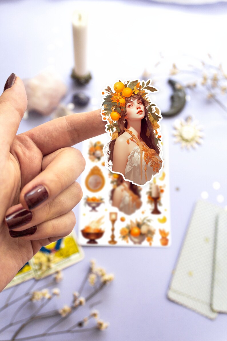 May include: A sticker sheet with a whimsical illustration of a woman with a crown of oranges and leaves. The sheet also includes smaller illustrations of oranges, candles, and other decorative elements.