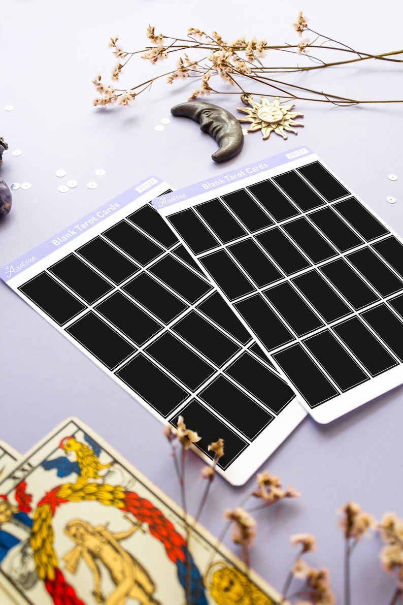 May include: Two sheets of blank tarot cards with black rectangles, labeled "Blank Tarot Cards" in white text. The cards are on a light purple surface, with decorative elements including a crescent moon, sun, and dried flowers.
