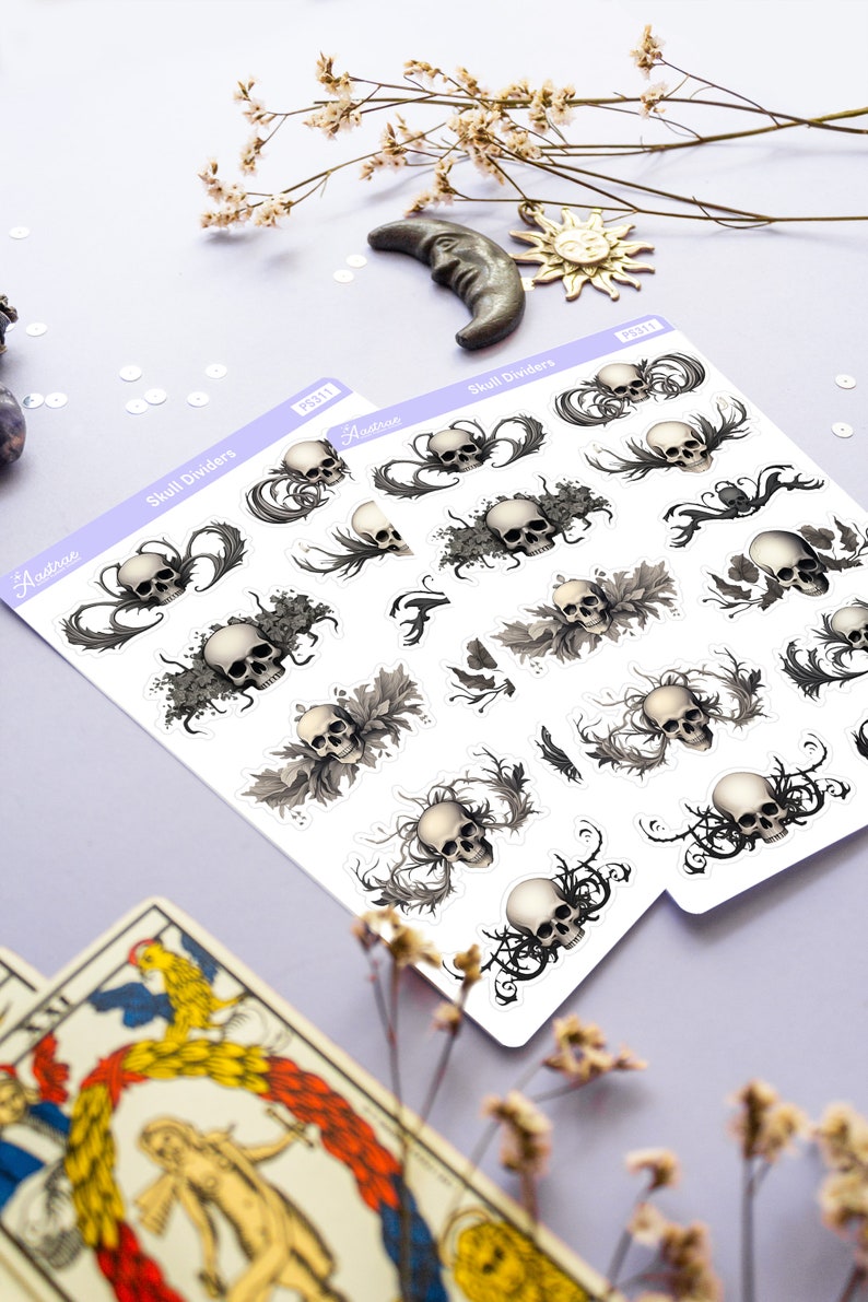 May include: Two sheets of stickers with a skull and floral design. The stickers are white with black and gray details. The text on the stickers reads "Skull Dividers" and "Aestrea".
