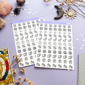 May include: Two sheets of white sticker paper with black witch-themed icons. The icons include a cauldron, a moon, a crystal, a book, a candle, and a hand holding a crystal. The sticker sheets are labeled "Witch Icons" and "PS134".