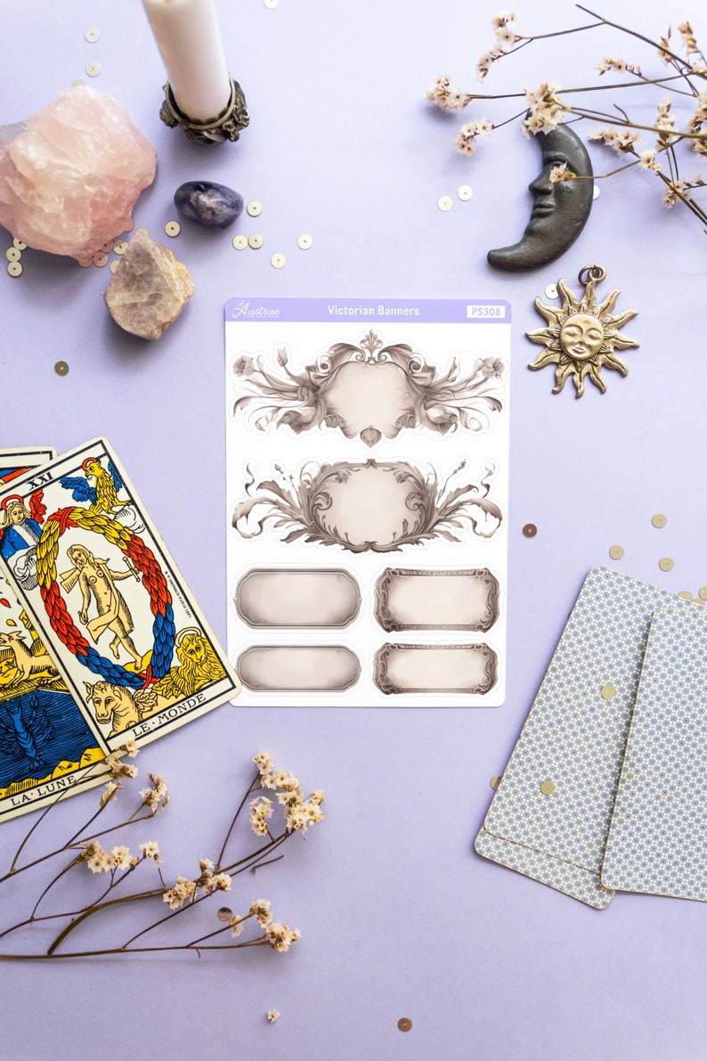 K&ouml;nnte beinhalten: Eine Blatt mit viktorianischen Banner-Aufklebern mit verzierten Rahmen und leeren Bannern. Die Aufkleber befinden sich auf einem violetten Hintergrund mit Tarotkarten, Kristallen und Dekorationsartikeln.