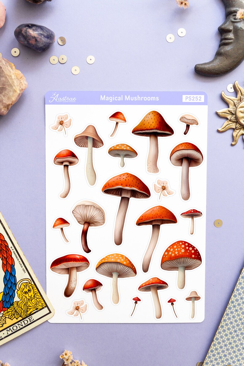 Peut inclure: Une feuille d'autocollants repr&eacute;sentant 15 illustrations de diff&eacute;rents champignons rouges et orange avec des points blancs. Les autocollants sont sur un fond blanc et la feuille est intitul&eacute;e "Champignons magiques" et "PS252".