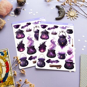以下が含まれることがあります： 紫と黒の炎、煙、星が描かれた魔女の釜のステッカーが2枚。ステッカーは、タロットカード、キャンドル、ドライフラワーが置かれた紫色の背景に貼られています。