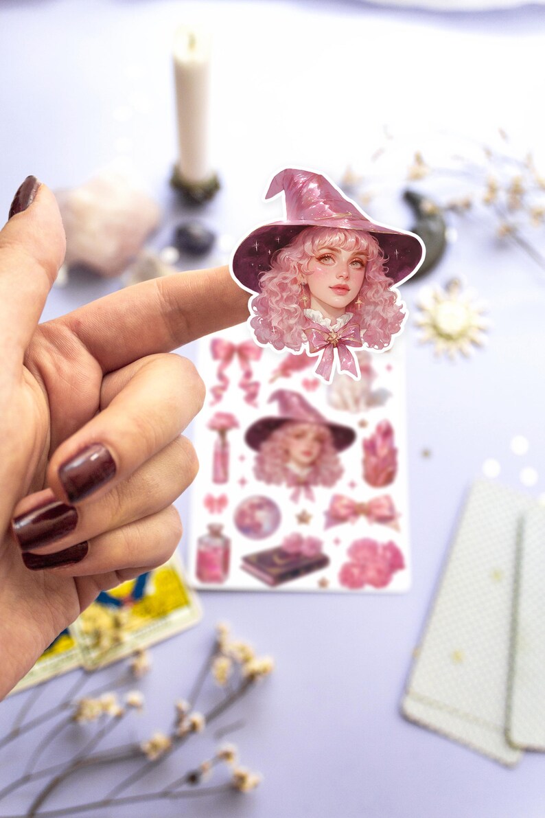 May include: A sheet of pink and white stickers featuring a witch with pink hair and a sparkly pink hat. The stickers also include other witchy elements like stars, moons, bottles, and flowers.