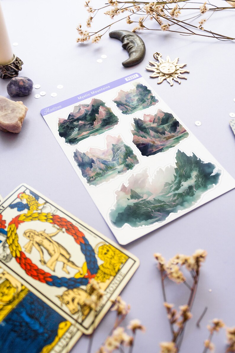 May include: A sheet of stickers featuring five watercolor illustrations of misty mountains. The stickers are on a white background and have a purple border. The text "Mystic Mountains" is printed on the sheet.