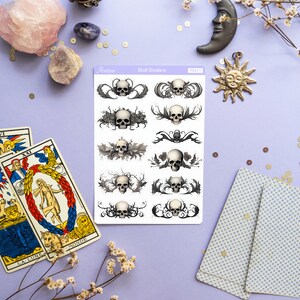 May include: A sheet of skull divider stickers with a white background and black and gray skull designs. The stickers are labeled "Skull Dividers" and "PS311".