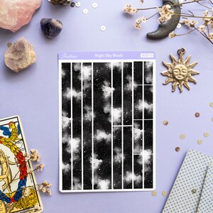 May include: A sheet of black and white washi tape with a night sky pattern. The tape is divided into 16 vertical strips. The pattern features white clouds and stars on a black background. The tape is labeled "Night Sky Washi" and "WS010".