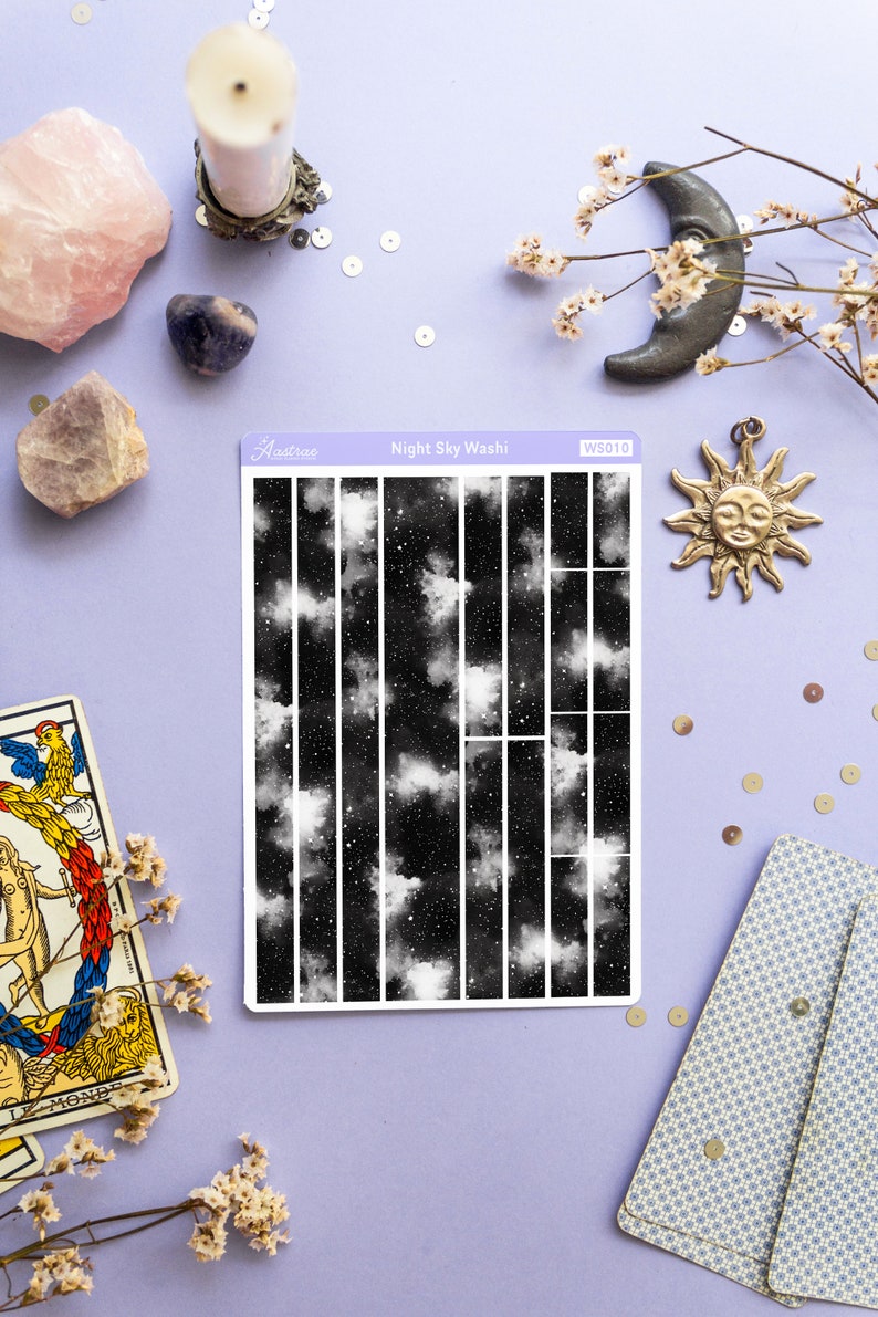 May include: A sheet of black and white washi tape with a night sky pattern. The tape is divided into 16 vertical strips. The pattern features white clouds and stars on a black background. The tape is labeled "Night Sky Washi" and "WS010".