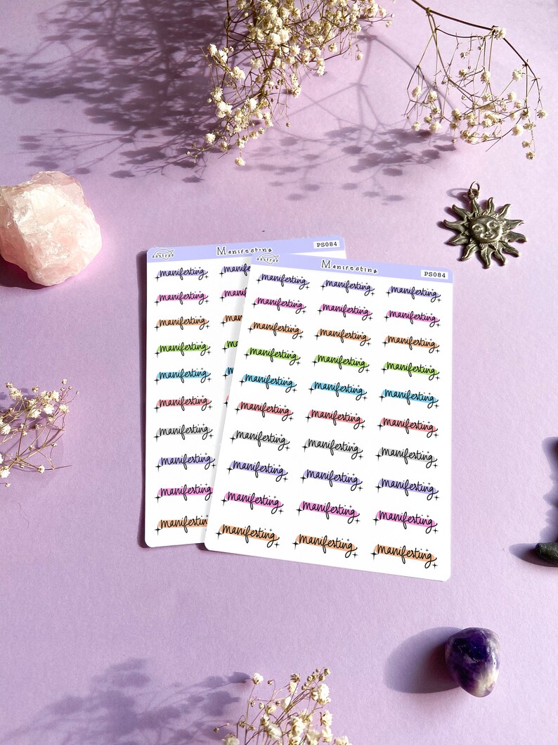 Puede incluir: Tres hojas de pegatinas con la palabra "manifesting" escrita en diferentes colores y estilos. Las pegatinas est&aacute;n sobre un fondo morado.