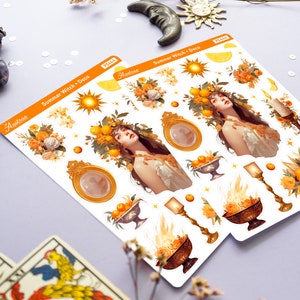 May include: A sheet of stickers featuring a summer witch theme. The stickers include a woman with a crown of lemons and oranges, a golden mirror, a sun, a candle, and a bowl of fruit. The stickers are on a white background with the text "Summer Witch Deco" and "Astrae" printed on the sheet.