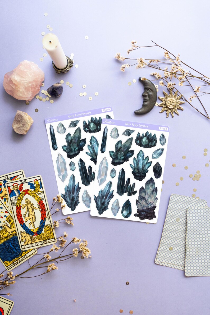 May include: Two sticker sheets with dark blue crystal designs, labeled "Dark Fairy Crystals", are displayed on a lavender surface. Other items include tarot cards, crystals, a candle, and decorative celestial objects.