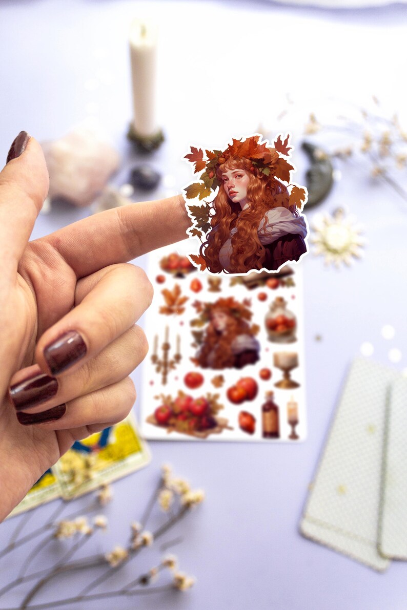 May include: A sheet of stickers featuring a woman with long red hair wearing a crown of autumn leaves. The stickers also include images of apples, candles, and a bottle of wine.