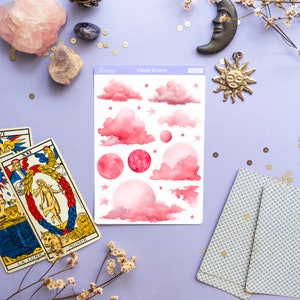 May include: A sheet of pink and white stickers with a cloudy dreams theme. The stickers feature pink clouds, stars, and moons. The sheet is labeled "Cloudy Dreams" and has a product number.