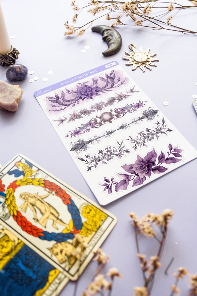 Peut inclure: Une feuille d'autocollants de s&eacute;parateurs floraux violets et gris avec le texte "Victorian Floral Dividers" et "Astrozee" sur la feuille. Les autocollants sont sur une surface violet clair avec une carte de tarot et des fleurs s&eacute;ch&eacute;es.