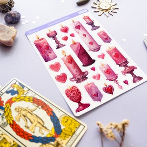 Pode incluir: Uma folha de adesivos com ilustra&ccedil;&otilde;es de velas de feiti&ccedil;o de amor rosa e roxas com cora&ccedil;&otilde;es. Os adesivos est&atilde;o em um fundo roxo claro. O texto "Love Spell Candles" est&aacute; impresso na folha.