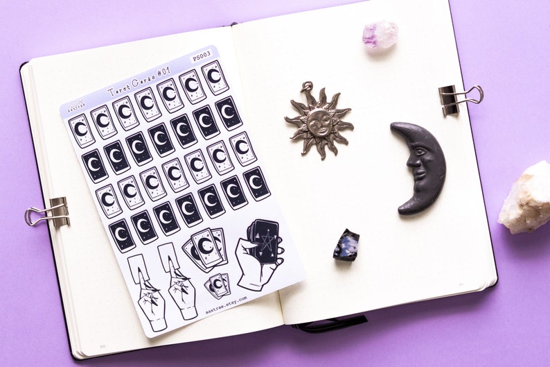 May include: A sheet of stickers featuring tarot card designs with a crescent moon and stars. The stickers are on a white background and are arranged in a grid pattern. The sheet also includes stickers of hands holding tarot cards. The text "Tarot Cards #01" and "PS003" is visible on the sheet.