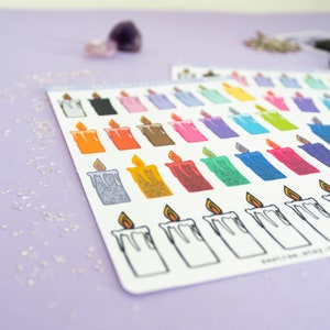 May include: A sheet of colorful candle stickers with a variety of colors and designs. The stickers are arranged in rows and columns on a white background. The sheet is on a purple surface.