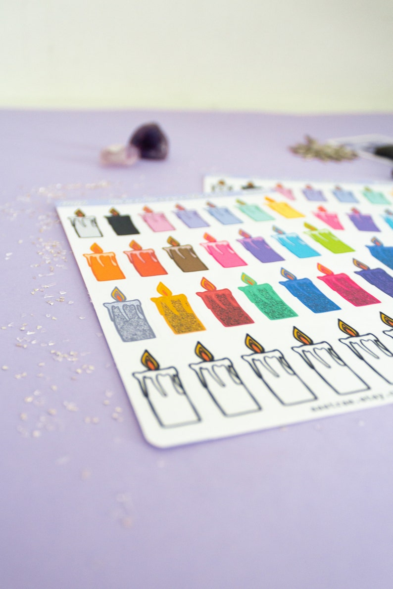 May include: A sheet of colorful candle stickers with a variety of colors and designs. The stickers are arranged in rows and columns on a white background. The sheet is on a purple surface.