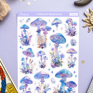 Puede incluir: Una hoja de pegatinas de setas iridiscentes con fondo blanco. Las pegatinas presentan varias setas azules y moradas con tallos blancos y una variedad de detalles florales. La hoja est&aacute; etiquetada como "Iridescent Mushrooms" y "PS465".