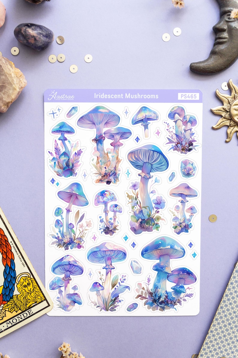 Puede incluir: Una hoja de pegatinas de setas iridiscentes con fondo blanco. Las pegatinas presentan varias setas azules y moradas con tallos blancos y una variedad de detalles florales. La hoja est&aacute; etiquetada como "Iridescent Mushrooms" y "PS465".