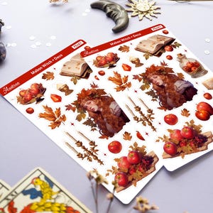May include: Two sheets of stickers featuring a witch with red hair and a crown of leaves, apples, a book, candles, and other autumnal elements. The stickers are labeled "Mabon Witch + Deco" and "PS467".