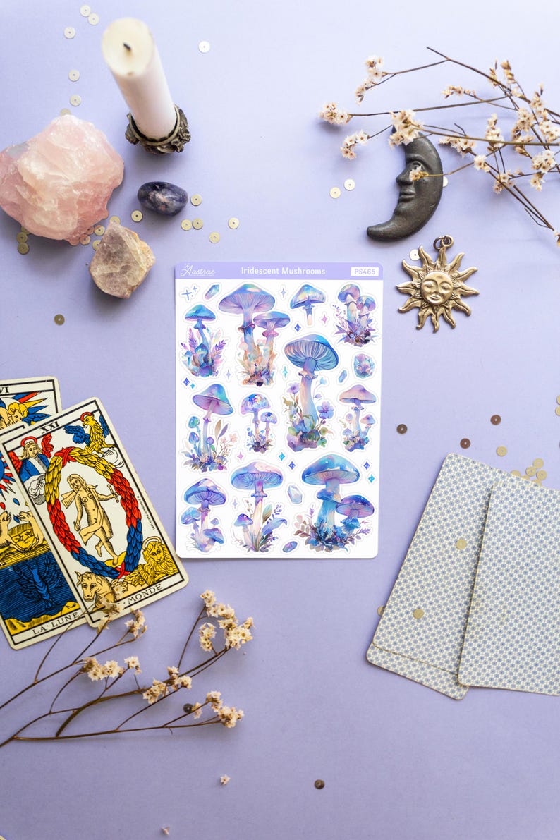 Puede incluir: Una hoja de pegatinas de setas iridiscentes con fondo blanco. Las pegatinas presentan varias setas azules y moradas con puntos blancos y un acabado brillante. La hoja est&aacute; etiquetada como "Iridescent Mushrooms" y "PS463".