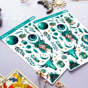May include: A sheet of stickers featuring a green and gold colour scheme with a Taurus zodiac sign, a crescent moon, stars, and a woman with horns and green hair. The text "Taurus + Deco" and "Astrae" are visible on the sticker sheet.