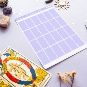 May include: A sheet of blank tarot cards with a lavender grid pattern, labeled "Blank Tarot Cards". The image includes a vintage tarot card, a crescent moon, a sun charm, and dried flowers, all on a lavender surface.