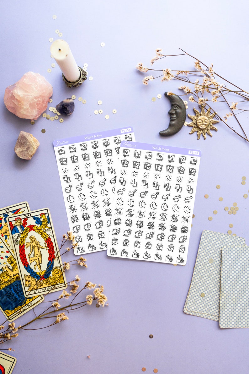 May include: Two sheets of stickers with witch icons. The stickers are white with black outlines and feature icons such as moons, stars, crystals, cauldrons, and books. The stickers are on a purple background with tarot cards, flowers, and crystals.