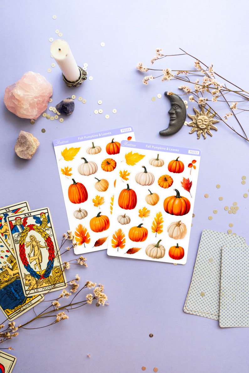 May include: Two sheets of stickers featuring fall-themed pumpkins and leaves. The stickers are on a light purple background with other fall-themed decorations, including a candle, crystals, tarot cards, and a small moon and sun.