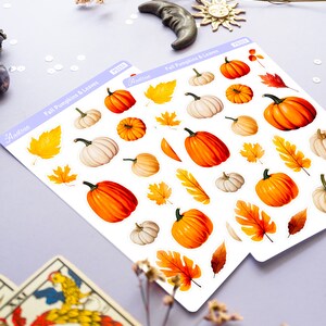 May include: Two sheets of stickers featuring fall-themed pumpkins and leaves. The stickers are white with a light purple border and the text "Fall Pumpkins & Leaves" printed on each sheet. The stickers are arranged in rows and include various sizes and colors of pumpkins and leaves.