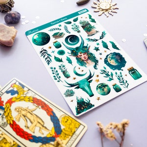 May include: A sheet of stickers featuring a green and gold colour scheme with a variety of celestial and nature-themed illustrations. The stickers include a moon, stars, leaves, a bull, a fairy, and a jar with glowing stars. The sheet is labelled "Taurus + Deco" and "Aastroe" with the product number "PS2111".