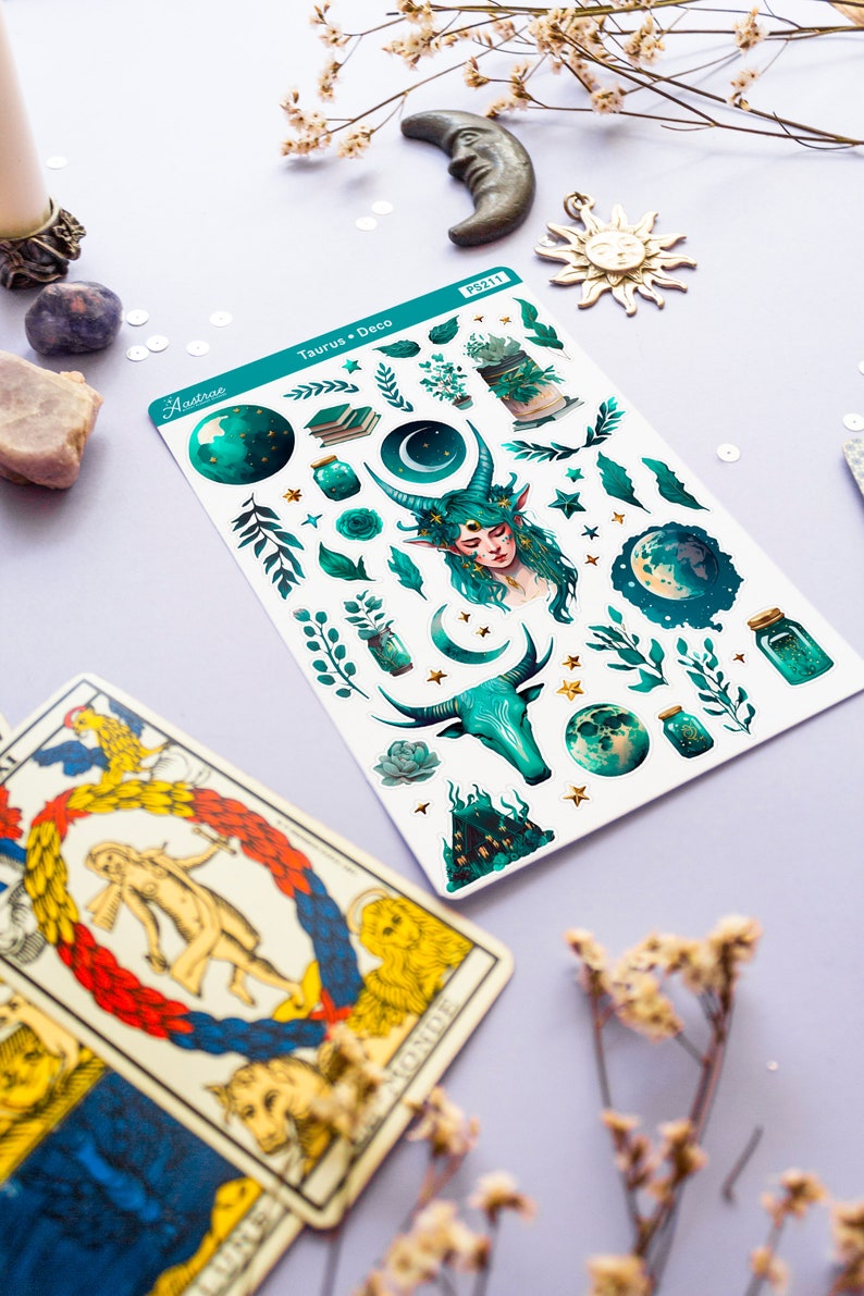 May include: A sheet of stickers featuring a green and gold colour scheme with a variety of celestial and nature-themed illustrations. The stickers include a moon, stars, leaves, a bull, a fairy, and a jar with glowing stars. The sheet is labelled "Taurus + Deco" and "Aastroe" with the product number "PS2111".
