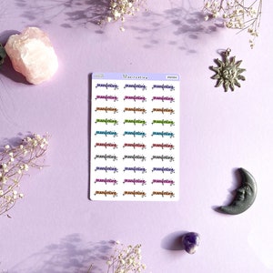 Puede incluir: Una hoja de pegatinas con la palabra "manifesting" escrita en diferentes colores y fuentes. Las pegatinas est&aacute;n sobre un fondo morado claro.