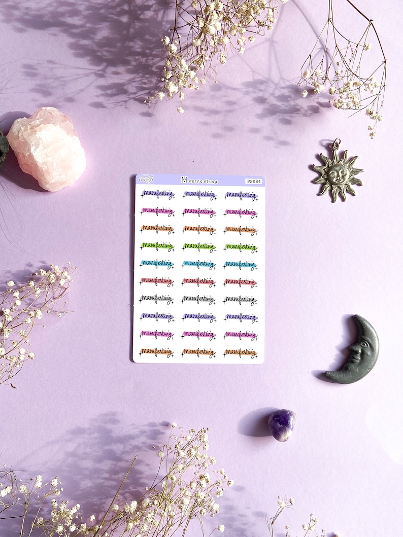 Puede incluir: Una hoja de pegatinas con la palabra "manifesting" escrita en diferentes colores y fuentes. Las pegatinas est&aacute;n sobre un fondo morado claro.
