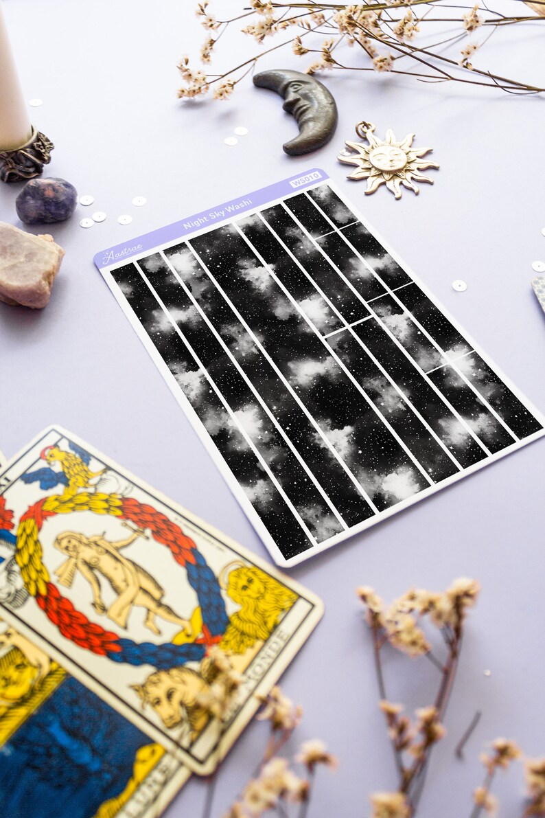 May include: A sheet of washi tape with a black and white night sky design. The tape is divided into 10 vertical strips, each with a different section of the night sky. The text "Night Sky Washi" is printed on the sheet.