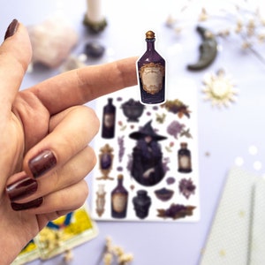 May include: A sticker sheet with a witch, potion bottles, and other magical elements. The sticker sheet is on a white surface and a finger is holding up a potion bottle sticker.