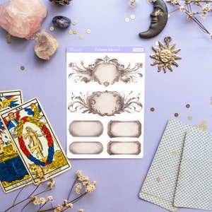 K&ouml;nnte beinhalten: Ein Bogen mit viktorianischen Banner-Aufklebern mit verzierten Rahmen und leeren Feldern zum Beschreiben. Die Aufkleber befinden sich auf einem violetten Hintergrund mit Tarotkarten, Kristallen und anderen Dekoartikeln.