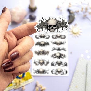 May include: A sheet of stickers featuring a skull with floral accents. The stickers are printed on white paper and are arranged in a grid pattern. The skull is surrounded by black vines and leaves.
