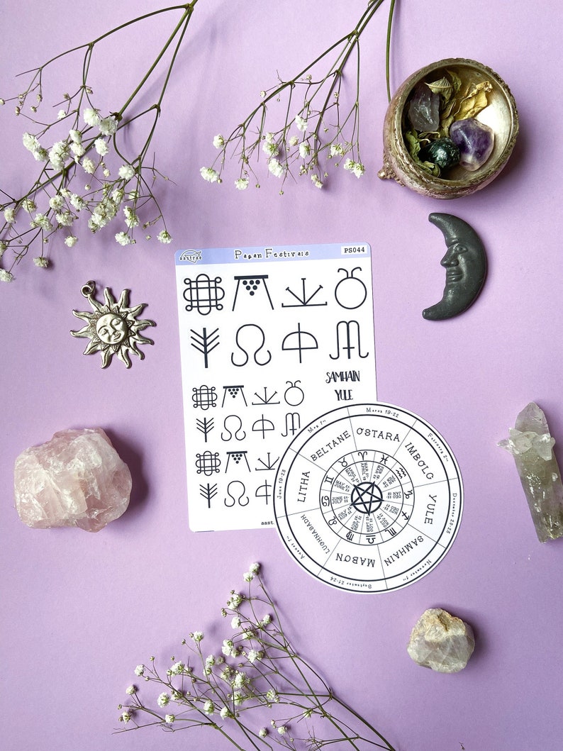 May include: A set of stickers featuring pagan symbols and a wheel of the year with the names of the eight sabbats. The stickers are on a purple background with white flowers, crystals, and a small cauldron.