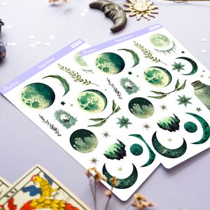 Puede incluir: Una hoja de pegatinas con fases lunares verdes y blancas, estrellas e ilustraciones bot&aacute;nicas. Las pegatinas est&aacute;n etiquetadas como "Sage Moon" y "Austera".