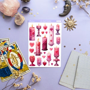 Pode incluir: Uma folha de adesivos com ilustra&ccedil;&otilde;es de velas rosa e roxas com detalhes dourados. Os adesivos s&atilde;o etiquetados como "Love Spell Candles" e "Aestree PS321".