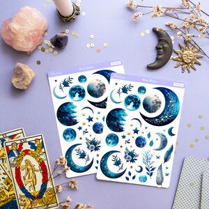 May include: Two sheets of blue moon themed stickers with a variety of blue moons, stars, and floral designs. The stickers are on a purple background with a candle, crystals, and tarot cards.