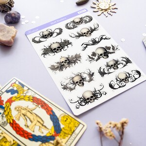 May include: A sheet of skull divider stickers with a white background. The stickers feature black and white illustrations of skulls with intricate floral designs. The sheet is labeled "Skull Dividers" and "Aestree".