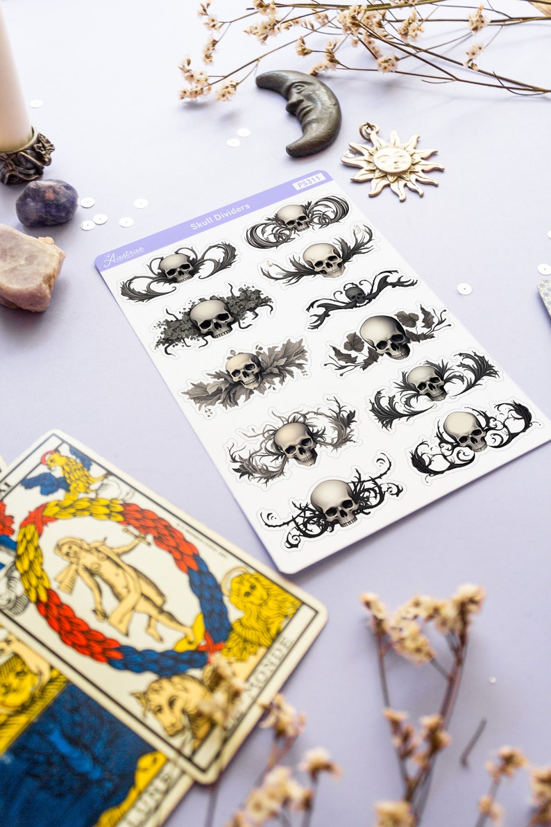 May include: A sheet of skull divider stickers with a white background. The stickers feature black and white illustrations of skulls with intricate floral designs. The sheet is labeled "Skull Dividers" and "Aestree".