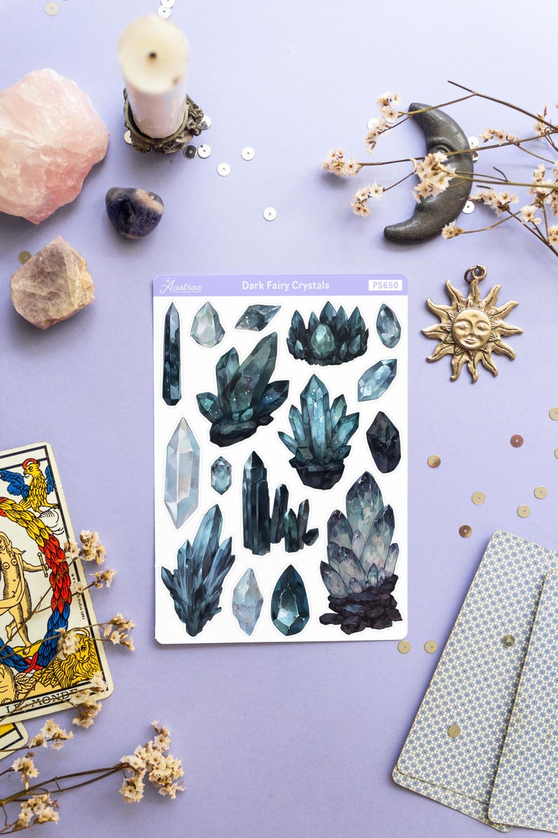 May include: A sheet of stickers labeled "Dark Fairy Crystals" featuring watercolor illustrations of dark blue and teal crystals. The image also includes a tarot card, a sun pendant, and other decorative elements.