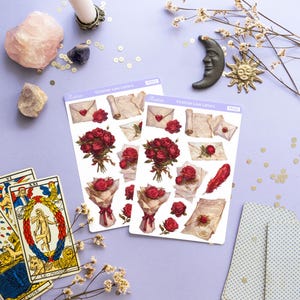May include: Two sheets of stickers featuring Victorian-era love letters, roses, and envelopes. The stickers are on a light purple background with gold glitter, a pink crystal, a white candle, a silver candlestick, a white flower sprig, a black crescent moon, and a gold sun.