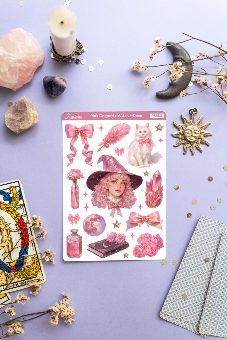 May include: A sheet of pink and white stickers featuring a pink-haired witch with a pink hat and a white cat. The stickers also include a pink bow, a feather, a crystal, a bottle of potion, a book, and a moon. The sheet is labeled "Pink Coquette Witch + Deco" and "PS553".