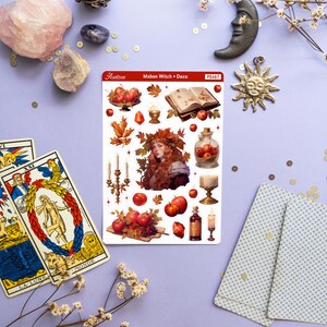 May include: A sheet of stickers featuring a witch with red hair and a crown of leaves, surrounded by apples, candles, and other autumnal imagery. The sticker sheet is titled "Mabon Witch + Deco" and has the number "PS467" printed on it.
